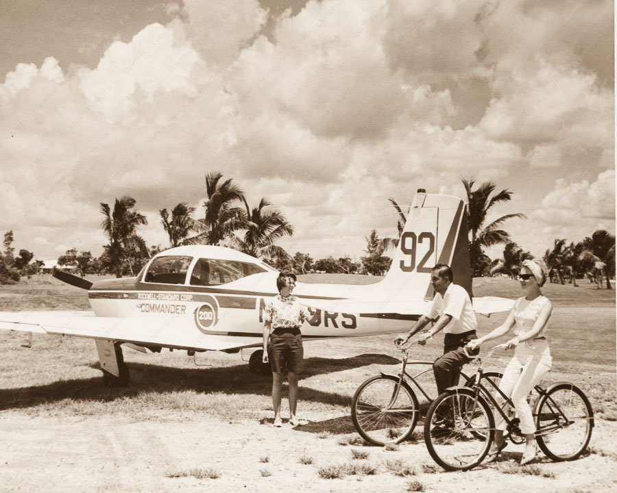 Rockwell Standard Corp. Commander 200 airplane parked at the air terminal and bicycle riders